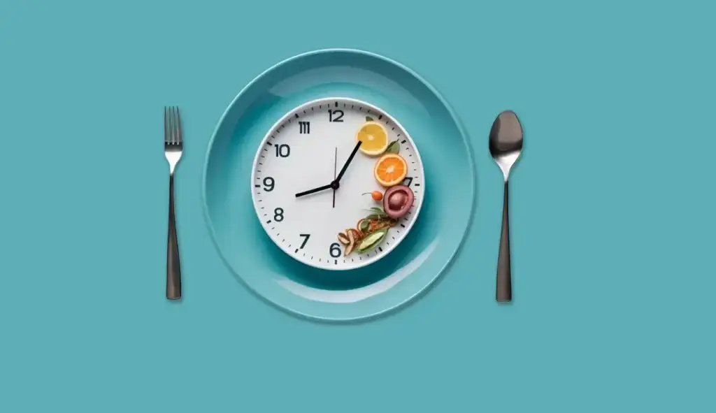 Clock face placed on a teal plate with fruit and vegetables around it, flanked by a fork and spoon to suggest mealtime.